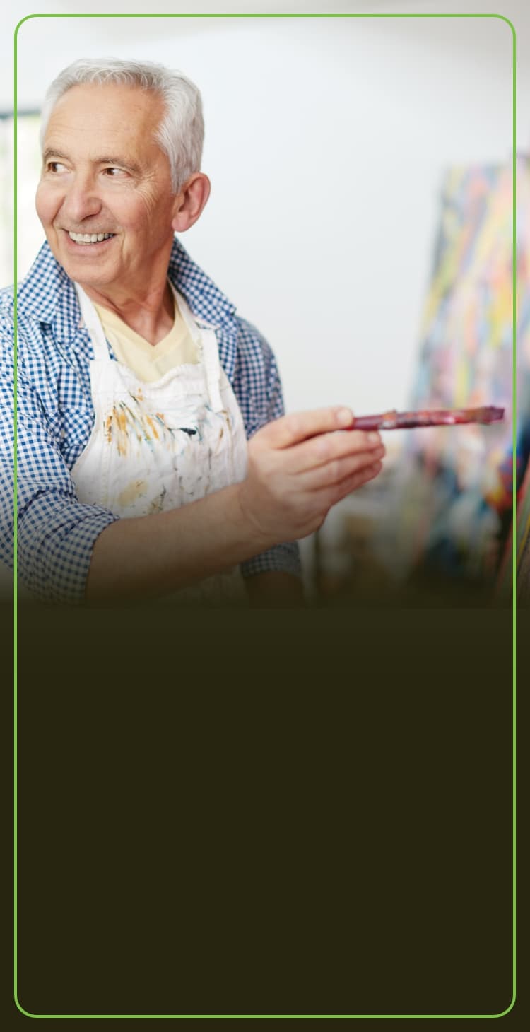 Man smiling as he holds a paint brush to the canvas